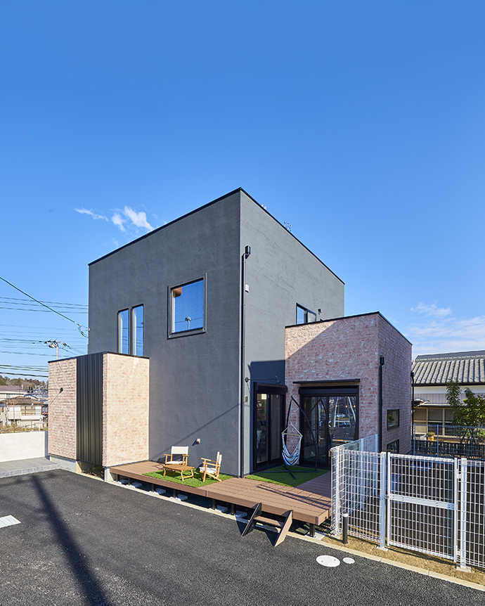 黒い塗り壁とウッドデッキが映えるモダンな外観の家